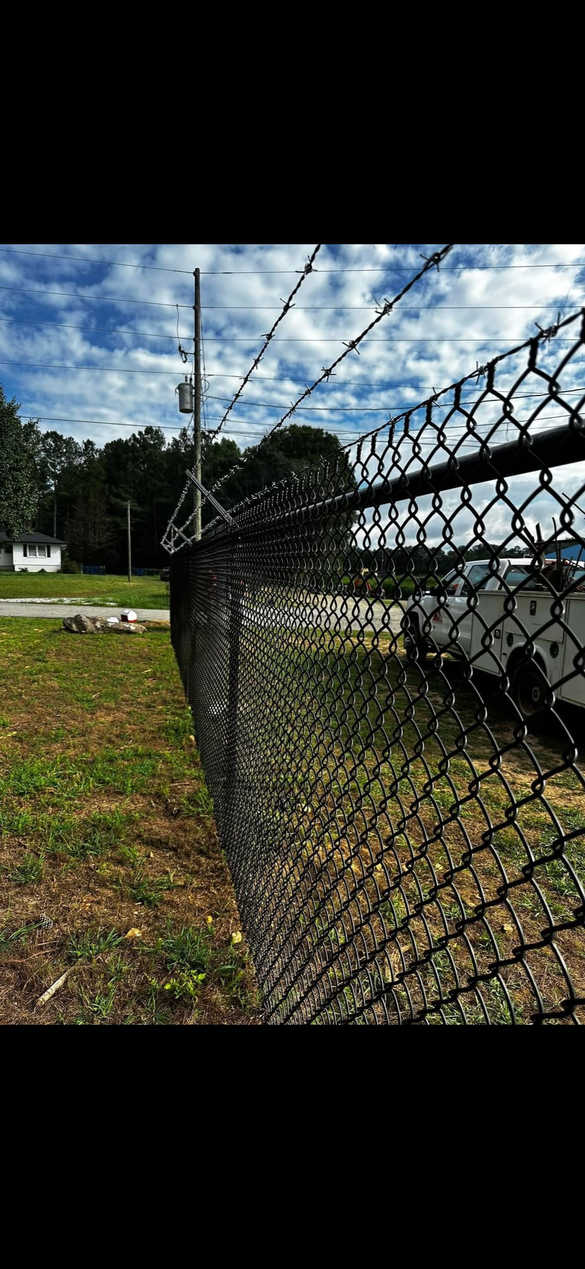 Black chain link fence with barbed-wire top installed by Fleming Fencing along a north Georgia property line