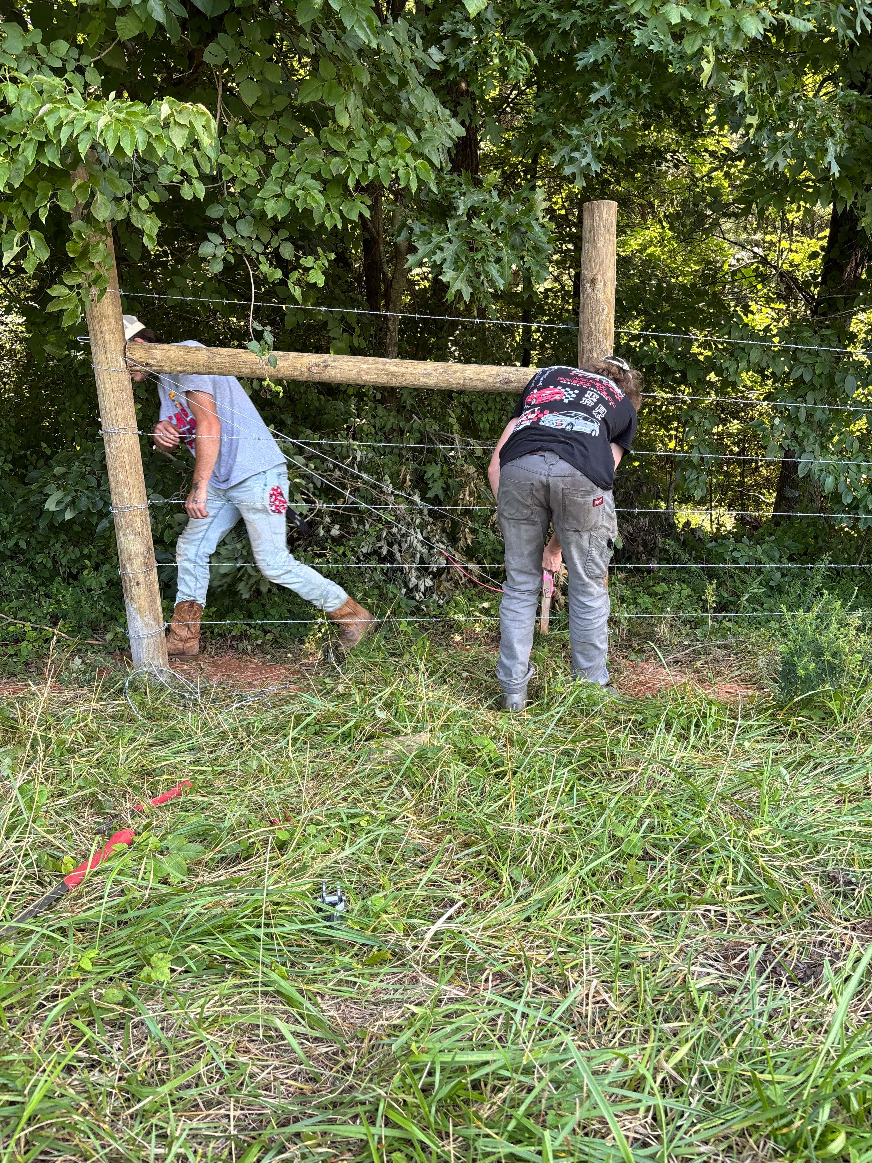 Fleming Fencing crew installing a barbed wire fence with wooden brace posts at a wooded property in north Georgia